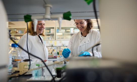 Image of two researchers in white lab coats smiling in the lab.