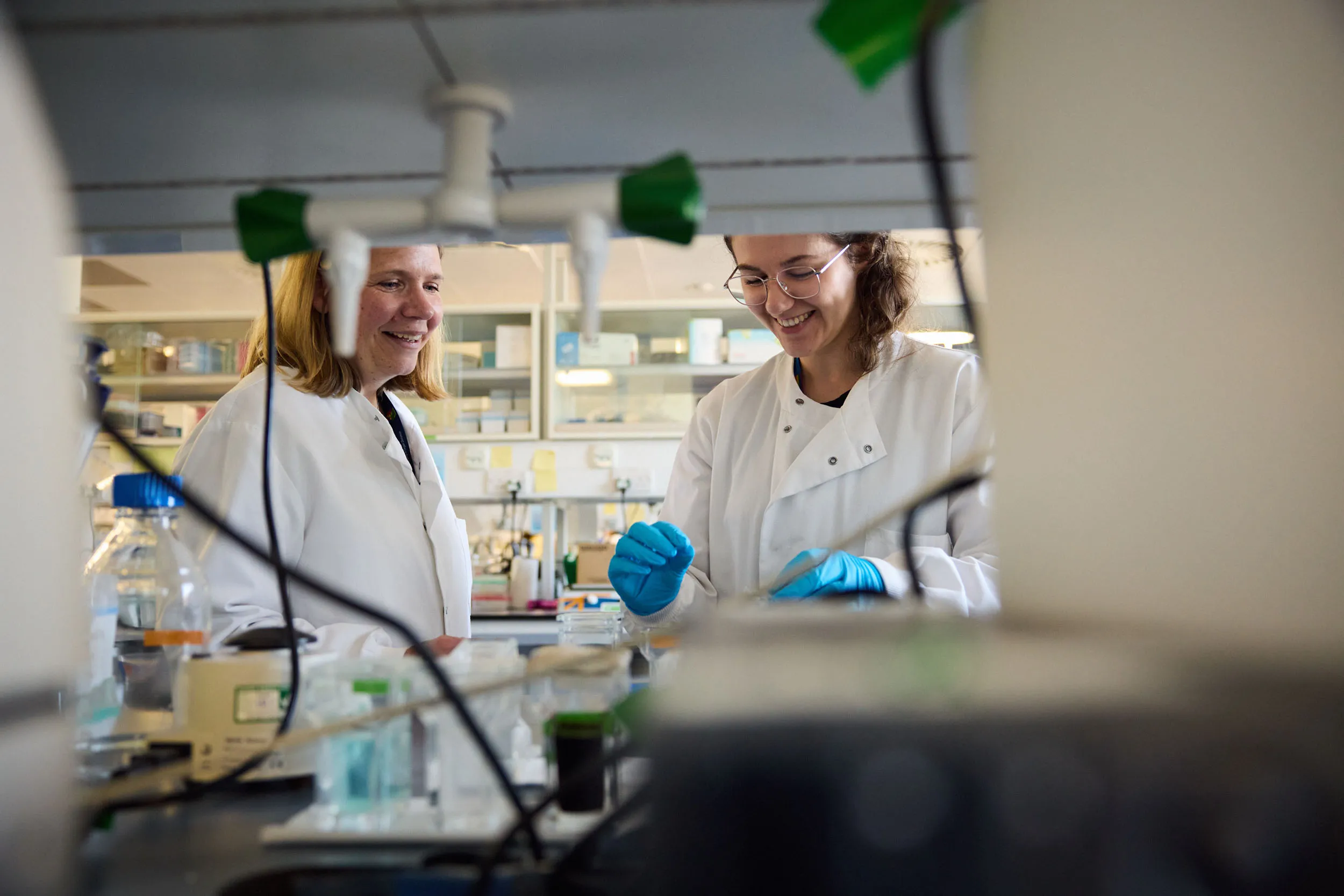 Image of two researchers in white lab coats smiling in the lab.