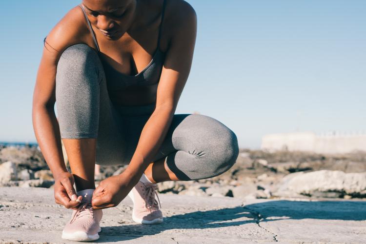 Woman wearing exercise clothing kneels to tie the laces of her running shoes